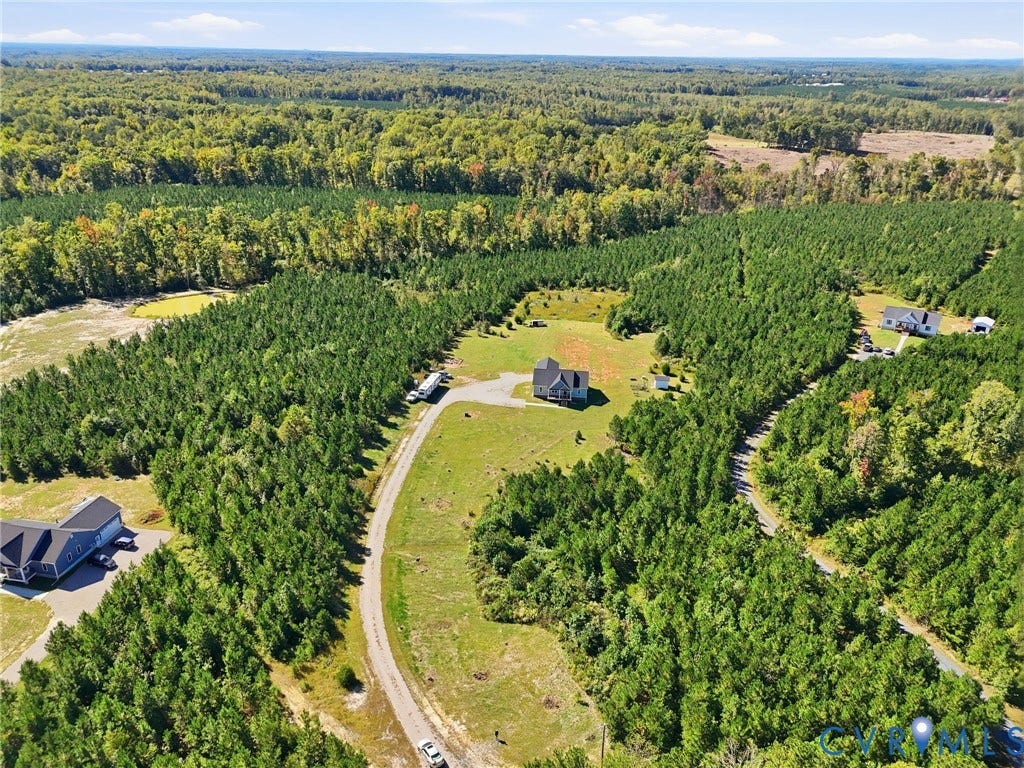 Expansive natural landscape featuring lush green trees, a distant water body, and multiple residential structures