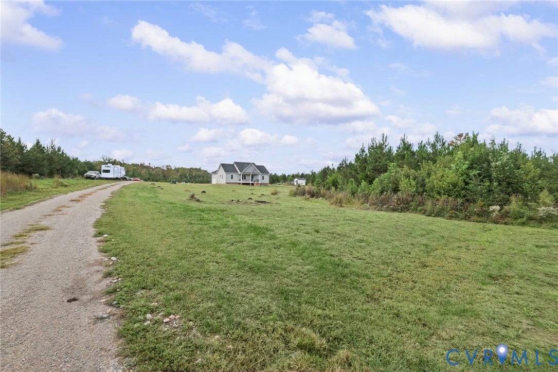 Expansive lot featuring a gravel driveway, mature trees, and a residential structure with a covered porch