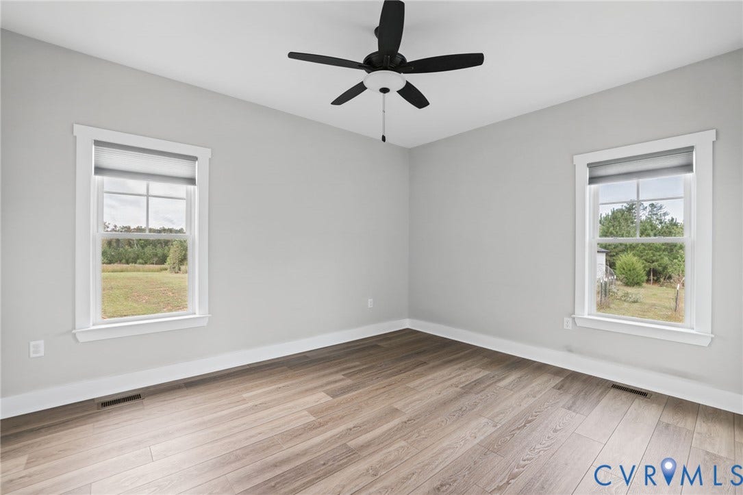 Bedroom 3, Light gray wall paint, wood-finish flooring, two windows with white trim, and a ceiling fan with light fixture