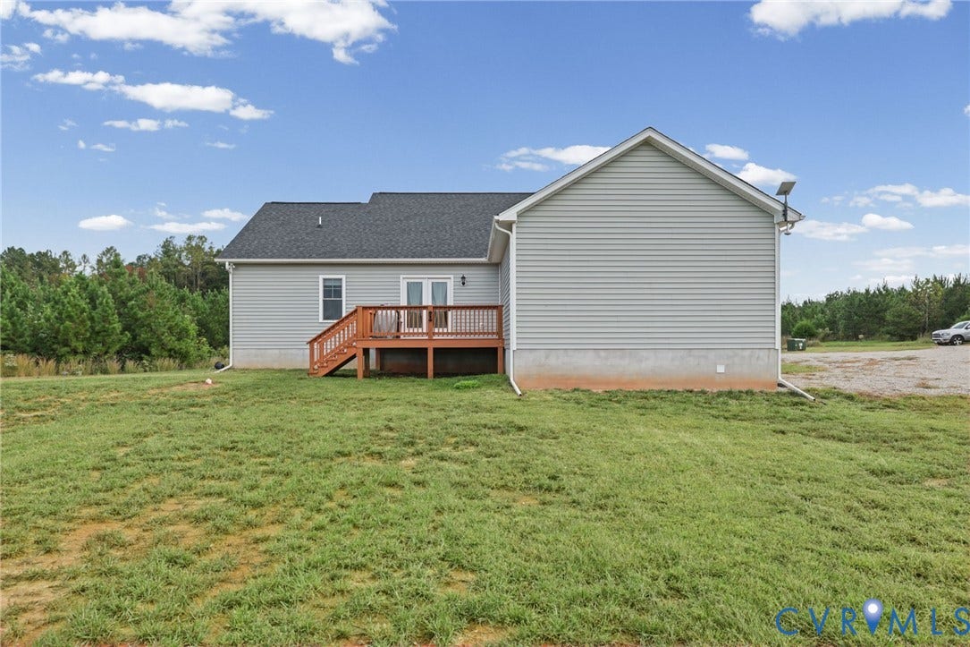 Expansive green space with a wood deck, light gray siding, and dark shingle roofing