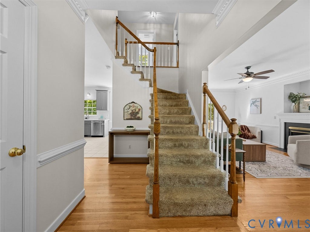 12000 Glen Kilchurn Drive, Chesterfield, VA 23838 Hardwood-style flooring throughout the main level, staircase with carpeted treads and wood banister, a living area with a ceiling fan, and a fireplace with a white mantel
