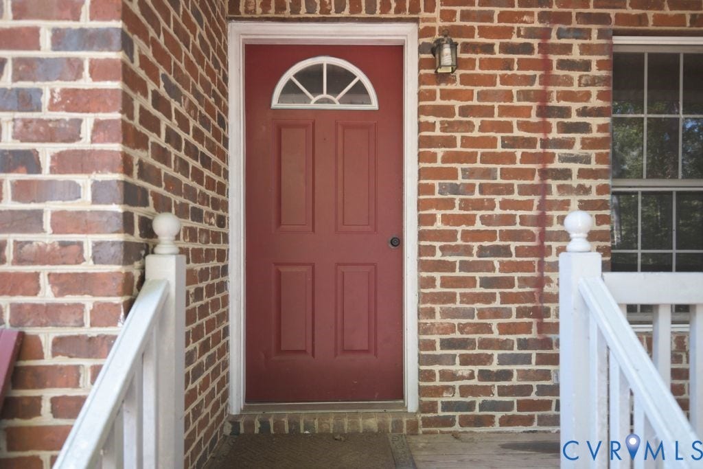Brick exterior featuring a paneled entry door with an arched transom, a traditional wall-mounted light fixture, and white painted railings