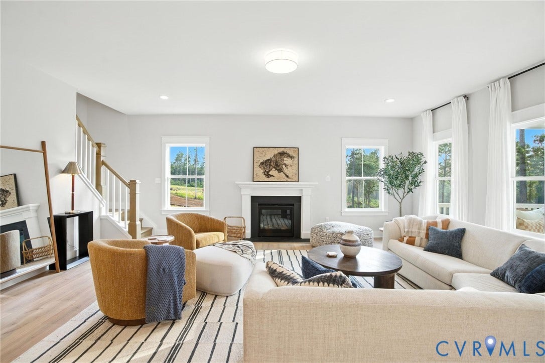 Lot 1 Needlewood Court, Olivet Church Estates, New Kent, VA 23124 Spacious open-concept living area featuring a fireplace with a white mantel, light wood-finish flooring, a contemporary ceiling light fixture, and multiple large windows