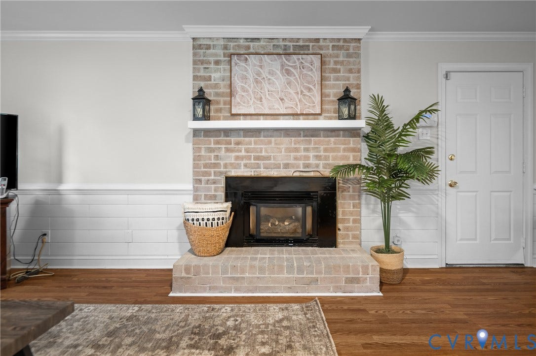 4525 Old Mesa Drive, North Chesterfield, VA 23237 Brick fireplace with a black firebox and a white mantel, complemented by wood-finish flooring and wainscoting