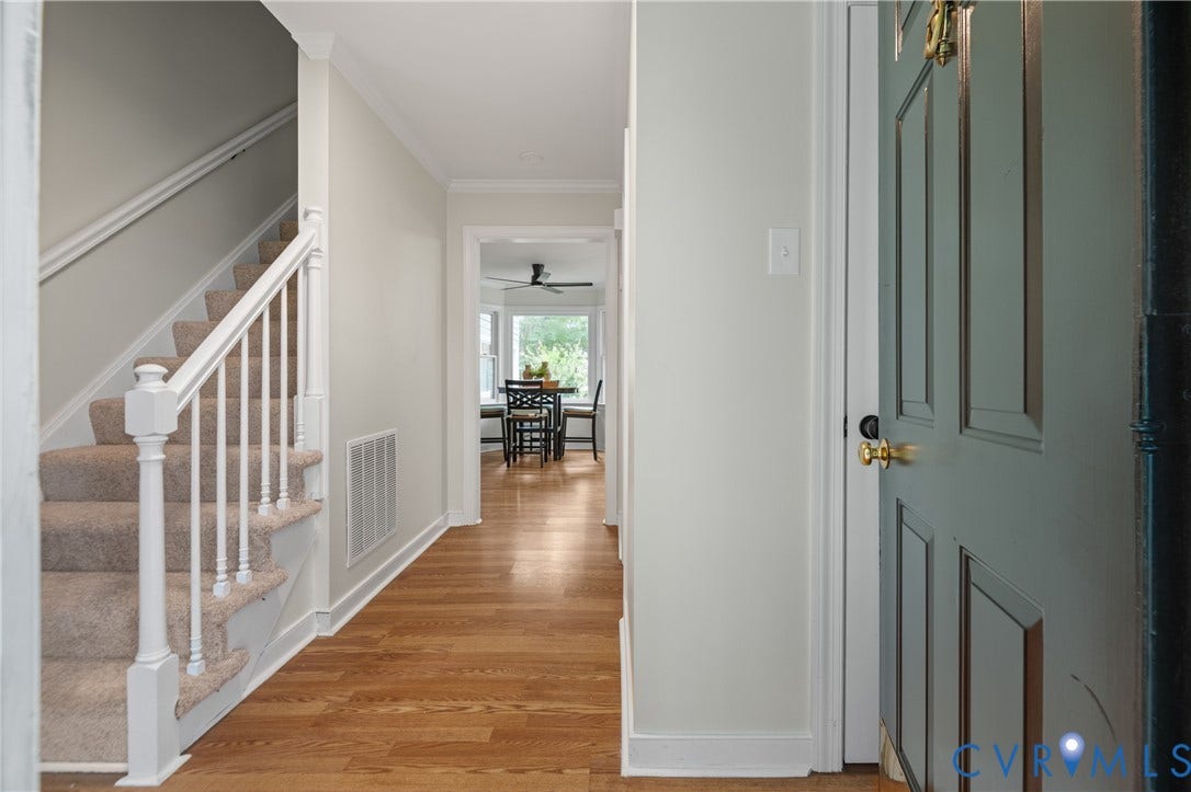 4525 Old Mesa Drive, North Chesterfield, VA 23237 Hardwood-style flooring in the entryway, staircase with carpeted treads and white banister, interior doorway with crown molding, panel door with brass hardware, and a ceiling fan visible in the background