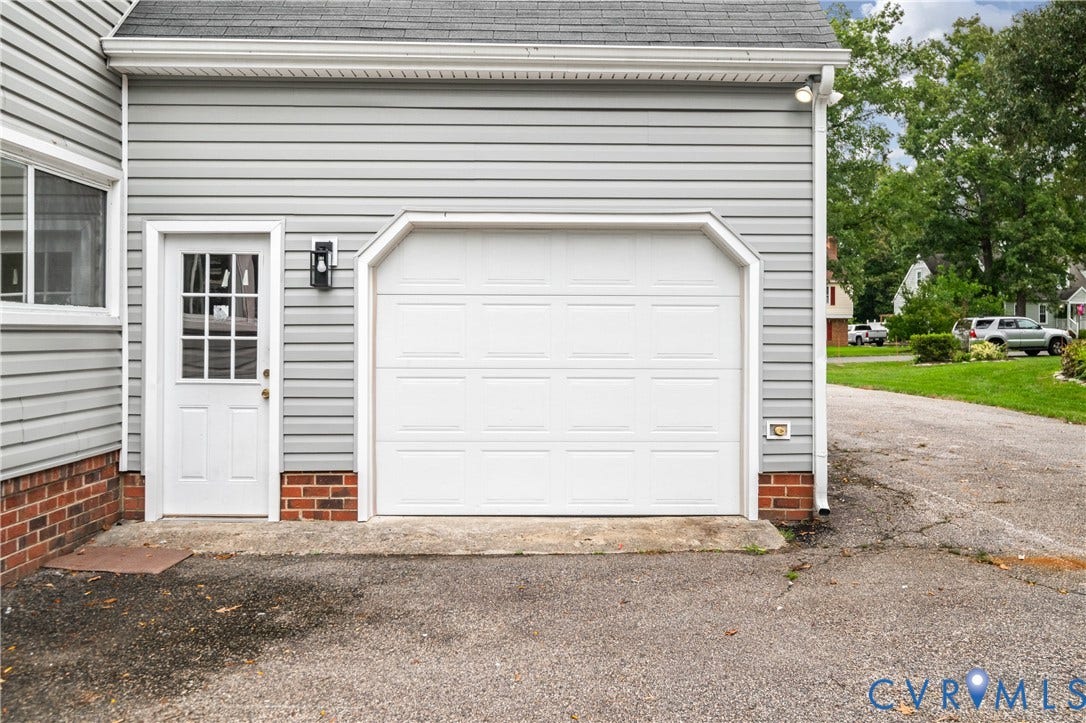 4525 Old Mesa Drive, North Chesterfield, VA 23237 Attached two-car garage with a panel door, featuring light gray horizontal siding and a white paneled entry door with glass inserts