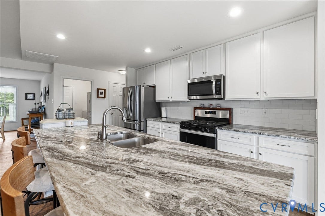 2927 Poorhouse Road, 522 Corridor, Goochland, VA 23063 Kitchen featuring an expansive island with a double basin sink, stainless steel appliances, white cabinetry, and a subway tile backsplash