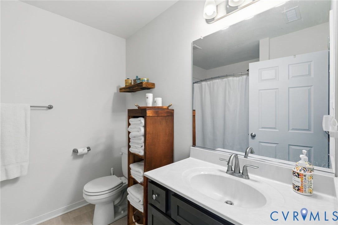 2927 Poorhouse Road, 522 Corridor, Goochland, VA 23063 Bathroom featuring a vanity with a white countertop and undermount sink, a large wall-mounted mirror, a toilet, a shower with a white curtain, and a wood-finish storage tower
