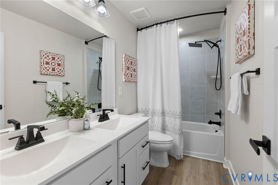8618 McKibben Drive, The Highlands, Chesterfield, VA 23838 Dual vanity with matte black fixtures, full-width mirror, light wood-finish flooring, tiled bath and shower combination, and built-in toilet