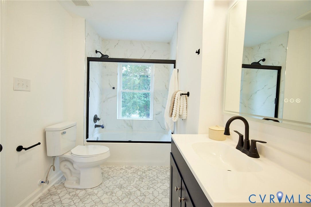 3103 Q St, Church Hill, Richmond, VA 23223 White bath surround with black-framed glass enclosure, white vanity with integrated sink, matte black faucet, and patterned floor tiling