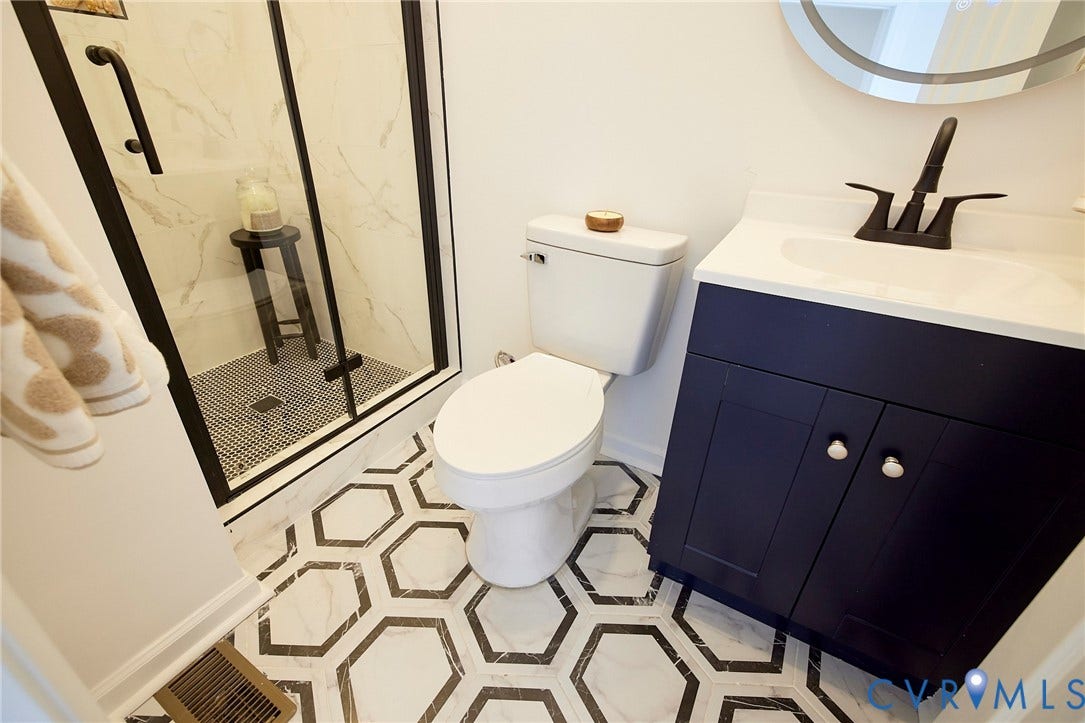 3103 Q St, Church Hill, Richmond, VA 23223 Hexagonal tile flooring, dark blue vanity with white countertop, black-framed glass shower enclosure, and a white toilet