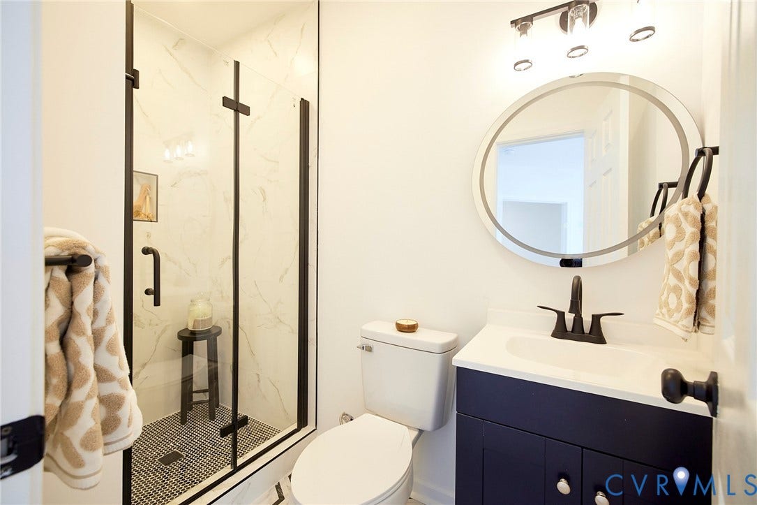 3103 Q St, Church Hill, Richmond, VA 23223 Glass-enclosed shower with subway tile and mosaic flooring, dark wood vanity with a white countertop and undermount sink, and a circular LED-backlit mirror