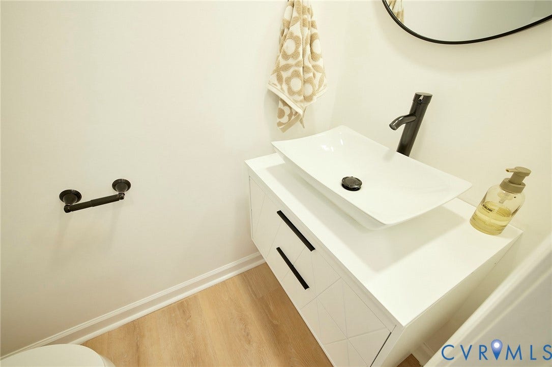 3103 Q St, Church Hill, Richmond, VA 23223 White vessel sink, wall-mounted faucet, floating vanity with black hardware, wood-finish flooring, and round mirror