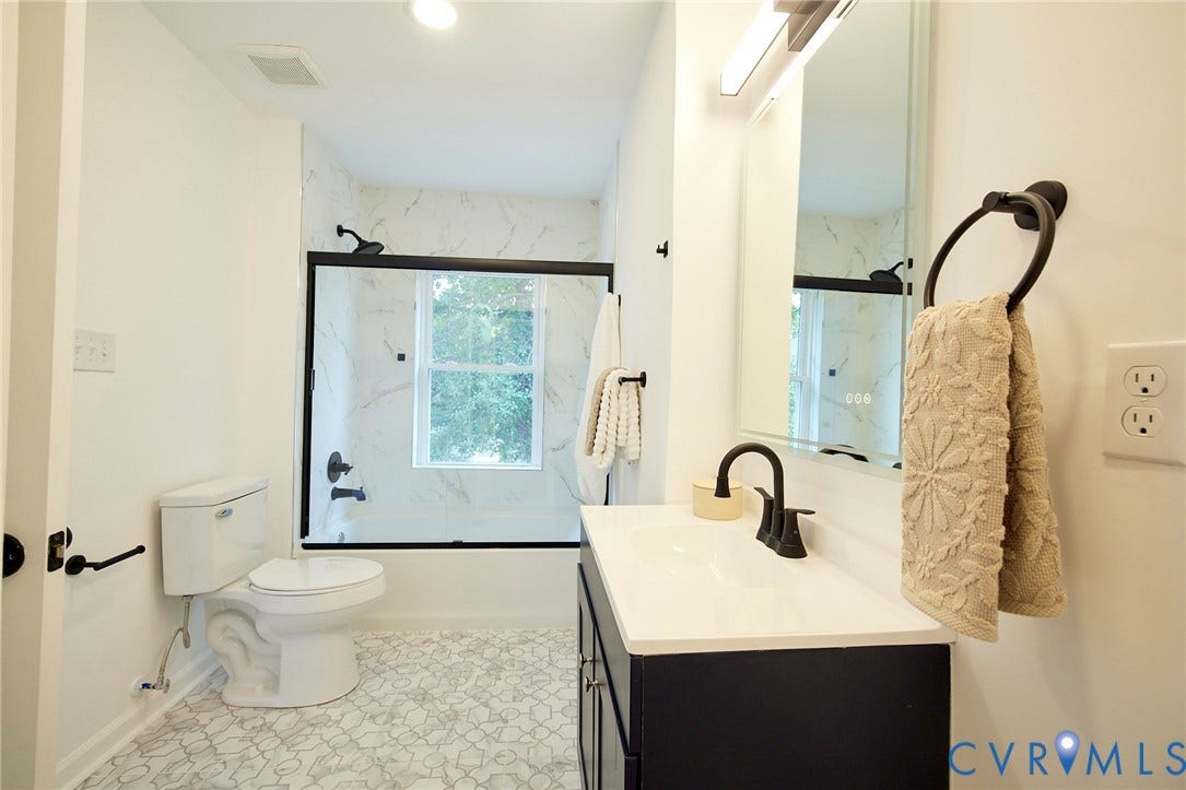 3103 Q St, Church Hill, Richmond, VA 23223 Bathroom featuring a shower-tub combination with glass enclosure, white vanity with integrated sink, black fixtures, and patterned floor tile