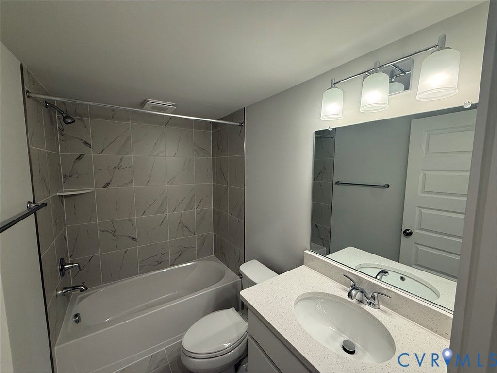 9452 belladdie Way, Glen Allen, VA 23059 Vanity with a quartz-finish countertop and undermount sink, three-light fixture, full-width mirror, and a tub with tiled surround