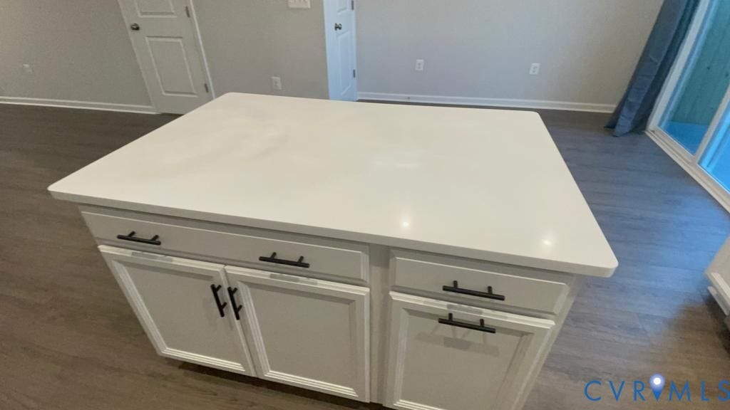 Kitchen island with white countertop, white cabinetry, matte black hardware, and wood-finish flooring