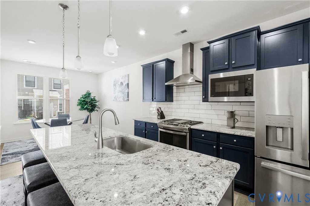 12221 Dutch Elm Circle, Midlothian, VA 23112 Kitchen featuring a large island with an integrated sink, pendant lighting, stainless steel appliances, dark blue cabinetry, and a white subway tile backsplash
