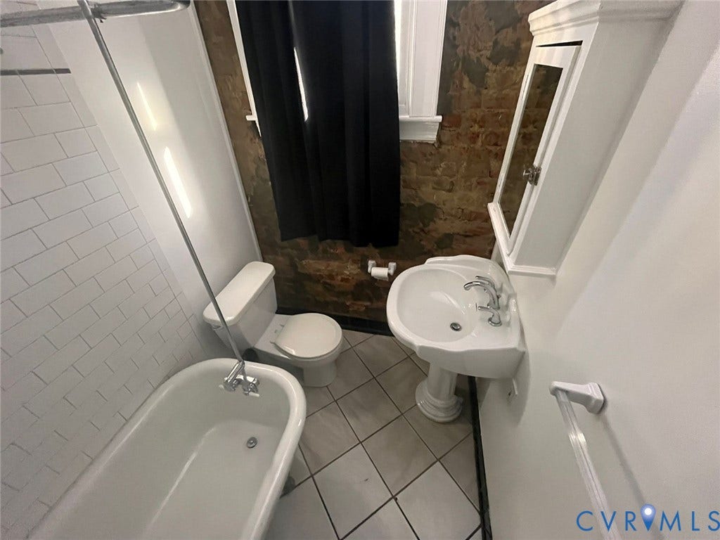 419 N 26th Street, #A, Richmond, VA 23223 Pedestal sink with chrome fixtures, white subway tile shower surround, clawfoot tub, exposed brick accent wall, and tiled flooring