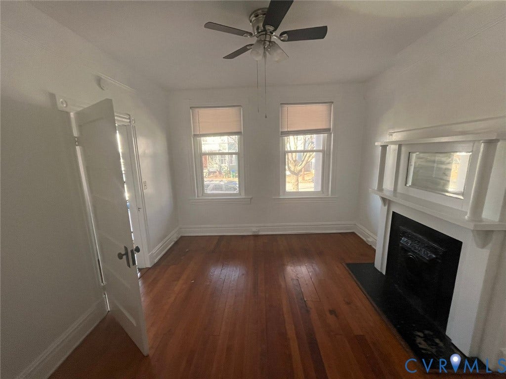 419 N 26th Street, #A, Richmond, VA 23223 Warm-toned wood-finish flooring, a decorative fireplace with a mantel, two windows, and a ceiling fan with integrated lighting