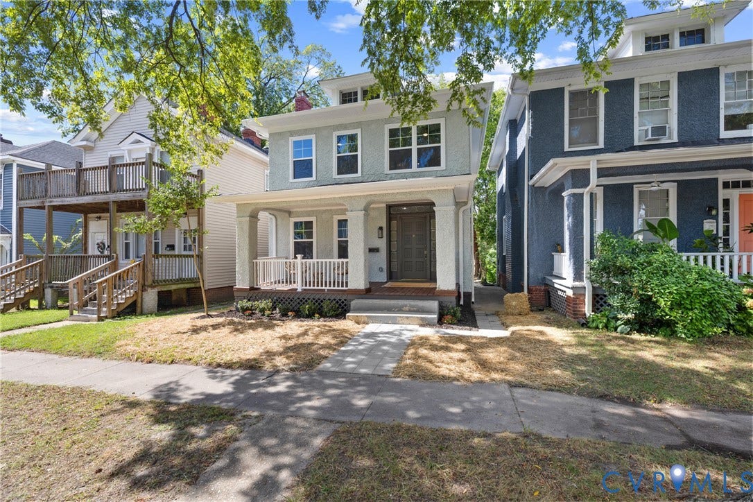 Two-story exterior with a light gray facade, a covered front porch with white railings, and a dark front door