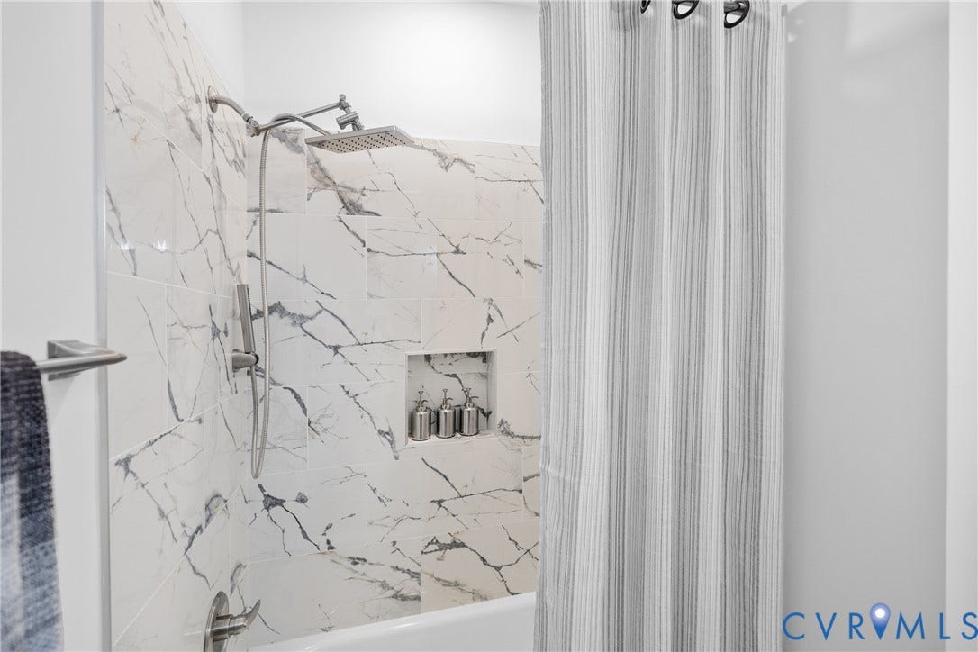 Bathtub with large format wall tiling, integrated shower niche, and a dual function shower head