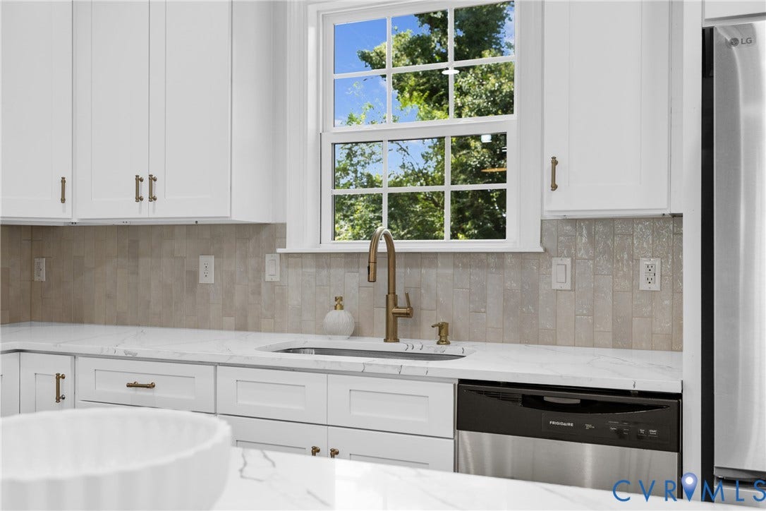 White cabinetry with brass-finish hardware, light-toned backsplash, quartz countertops, and an undermount sink with a brass-finish faucet