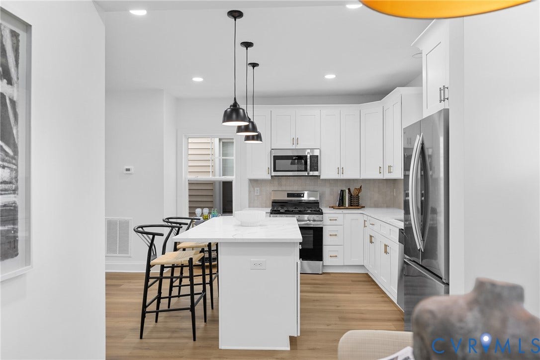 Kitchen featuring white cabinetry, stainless steel appliances, a center island with seating, pendant lighting, and wood-finish flooring