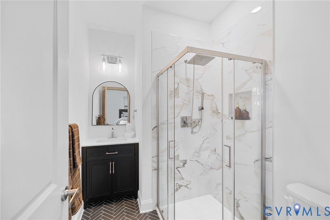Glass-enclosed shower with a rain shower head and marble-patterned tile surround