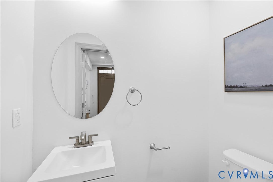 Pedestal sink with a single-handle faucet, oval mirror, and a wall-mounted toilet