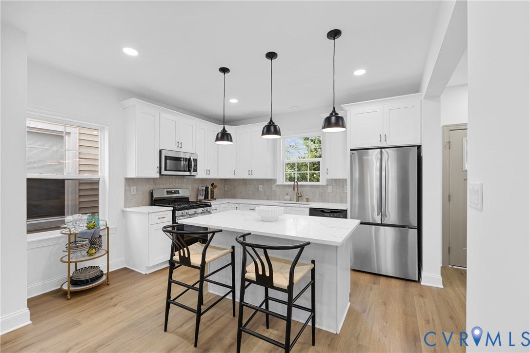 Kitchen featuring white cabinetry, stainless steel appliances, a center island with countertop seating, wood-finish flooring, and pendant lighting