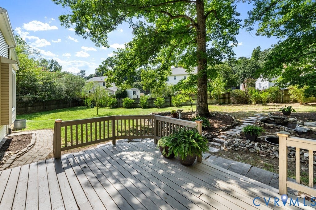 2416 Mountainbrook Drive, Crown Grant, Henrico, VA 23233 Expansive wood deck with a full railing, overlooking a large grassy lawn, mature trees, and a stone path leading to a water feature