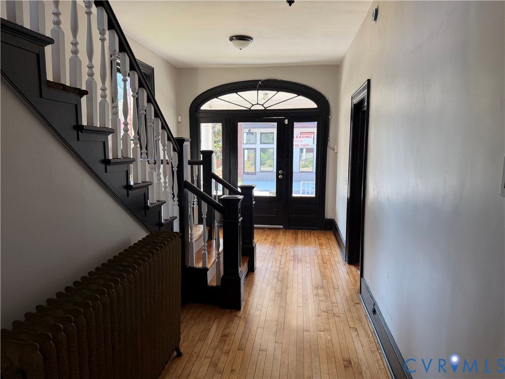 715 High Street, Petersburg, VA 23803 Hardwood flooring, classic staircase with painted balusters, arched entry door with transom window, and a vintage radiator