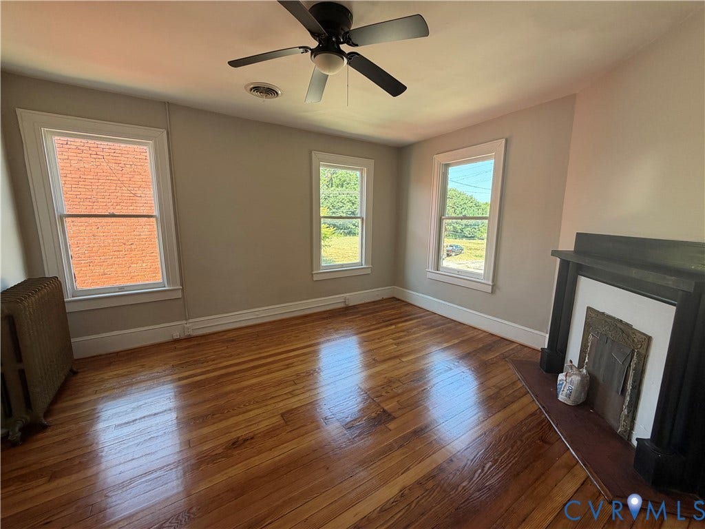 715 High Street, Petersburg, VA 23803 Hardwood flooring, painted walls, three windows with white trim, a ceiling fan, and a decorative fireplace with a dark wood mantel