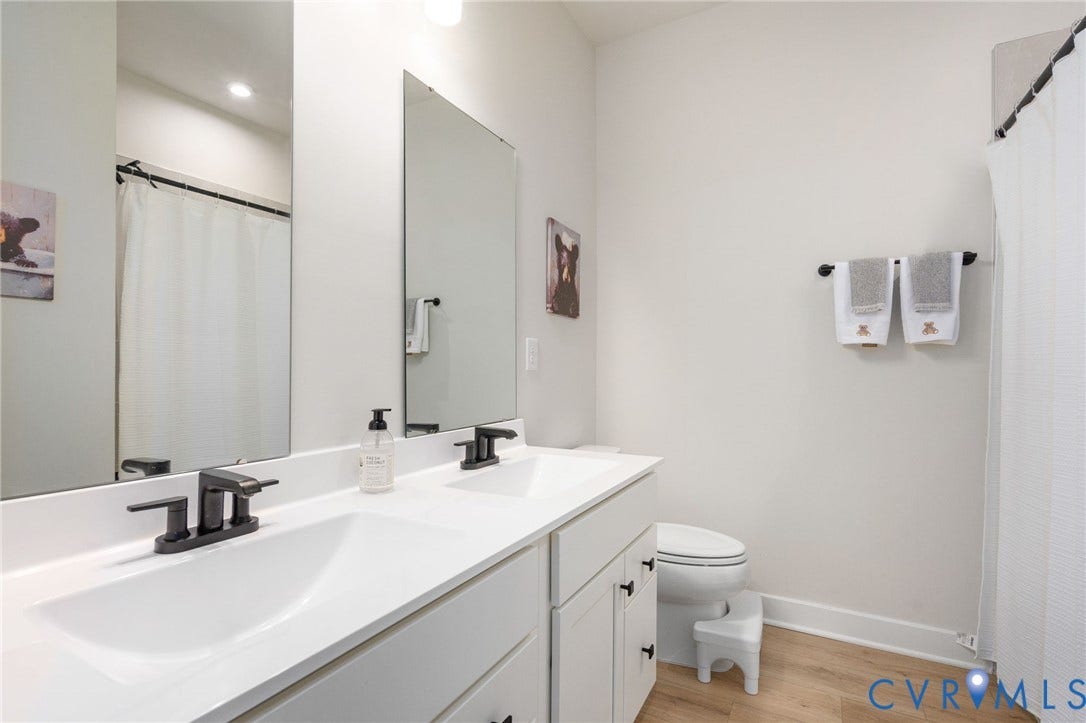 8045 Lake Laurel Lane, #B, Laurel Oak Condos, Glen Allen, VA 23060 Dual vanity with integrated sinks, matte black fixtures, full-width mirrors, wood-finish flooring, and a white shower curtain