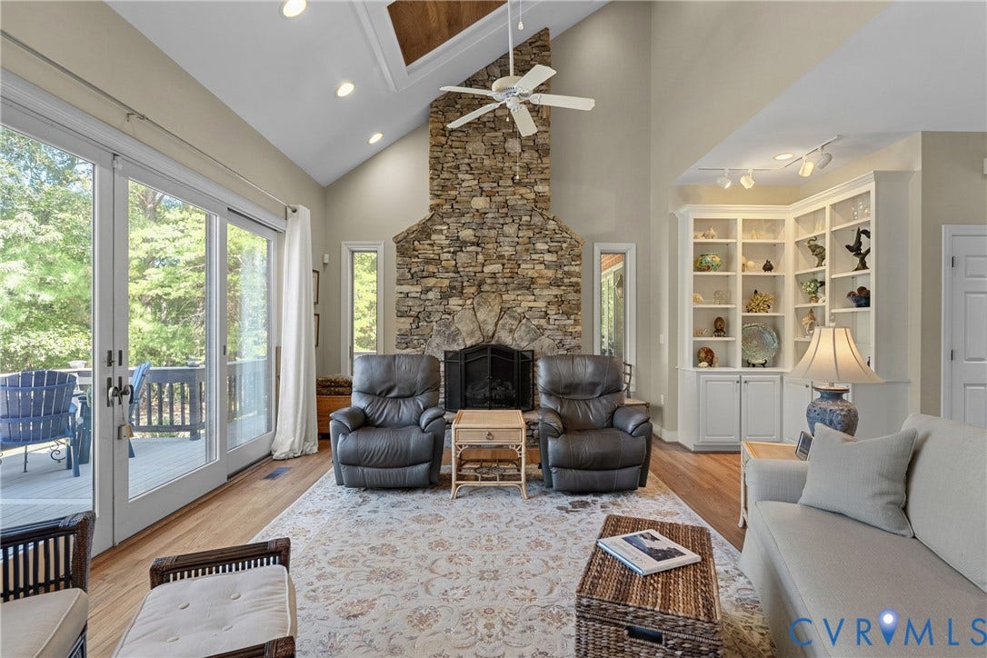 447 Tranquility Road, Reedville, VA 22539 Vaulted ceiling with wood-finish accent, stone fireplace, built-in shelving, wood-finish flooring, and sliding glass doors to outdoor deck