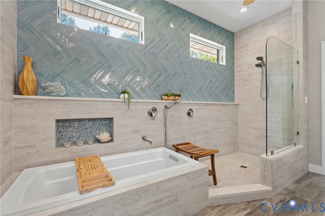 447 Tranquility Road, Reedville, VA 22539 Recessed bathtub with deck-mounted fixtures, walk-in shower with glass enclosure, wall-mounted shower system, and blue herringbone tile accent wall