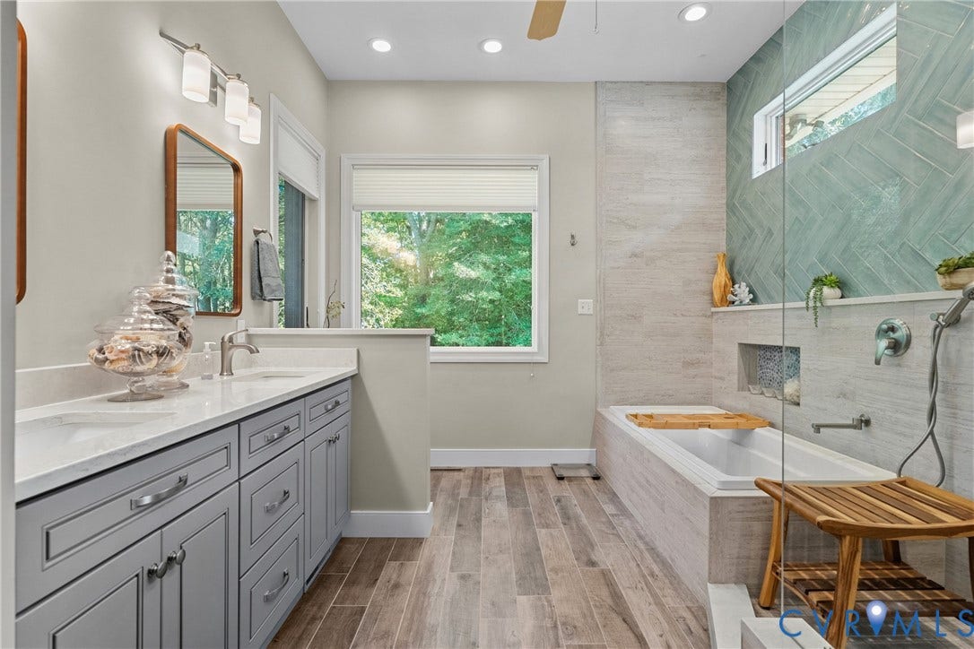 447 Tranquility Road, Reedville, VA 22539 Dual vanity with gray cabinetry and white countertops, wood-finish flooring, built-in soaking tub, glass-enclosed shower with tiled walls, and recessed lighting