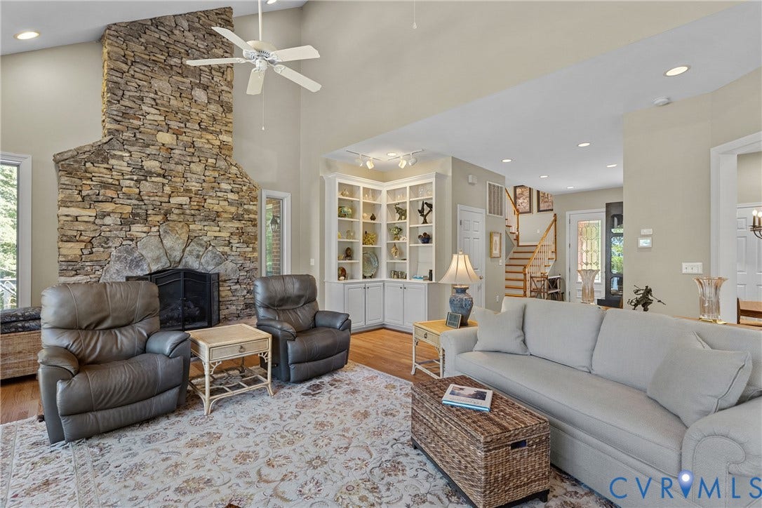 447 Tranquility Road, Reedville, VA 22539 Vaulted ceiling with a ceiling fan, stone fireplace, built-in shelving, hardwood flooring, and a staircase with a wood handrail
