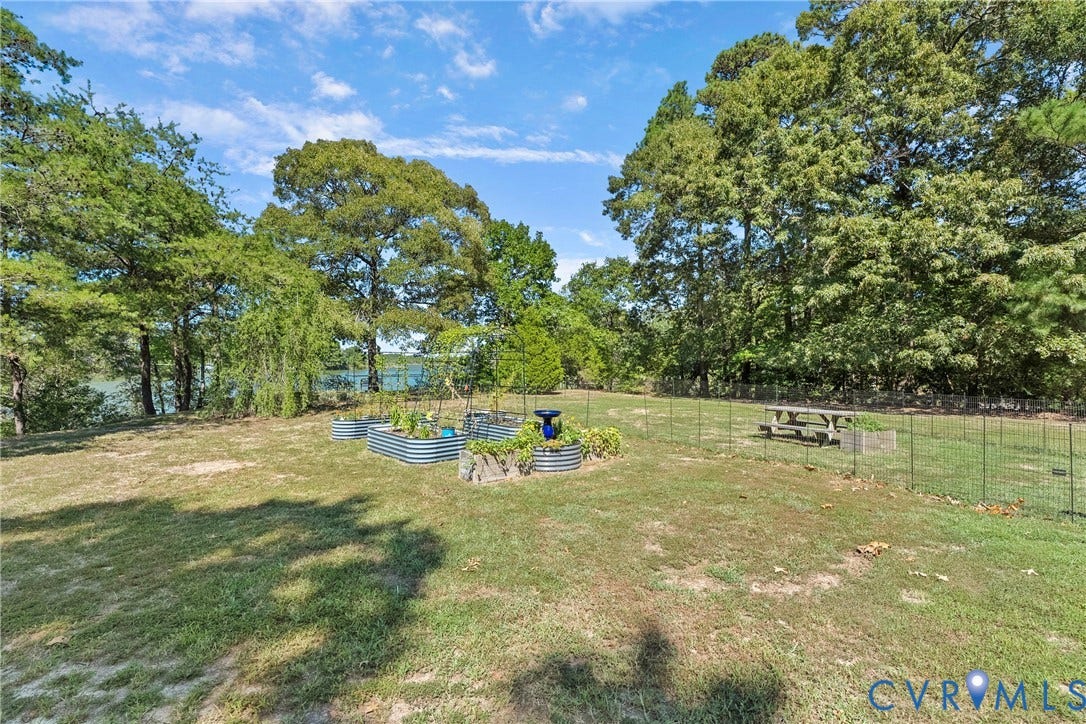 447 Tranquility Road, Reedville, VA 22539 Expansive yard featuring mature trees, raised garden beds, and a metal wire fence enclosure