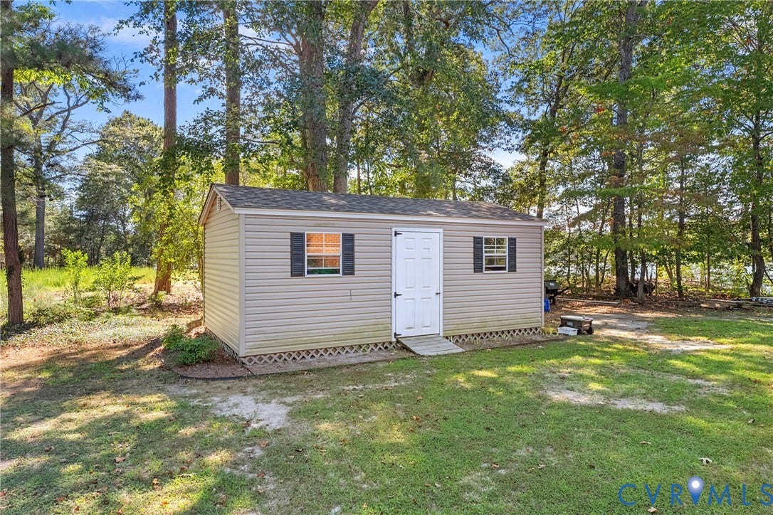 447 Tranquility Road, Reedville, VA 22539 Exterior storage shed with vinyl siding, white paneled door, two windows with shutters, and a wood ramp