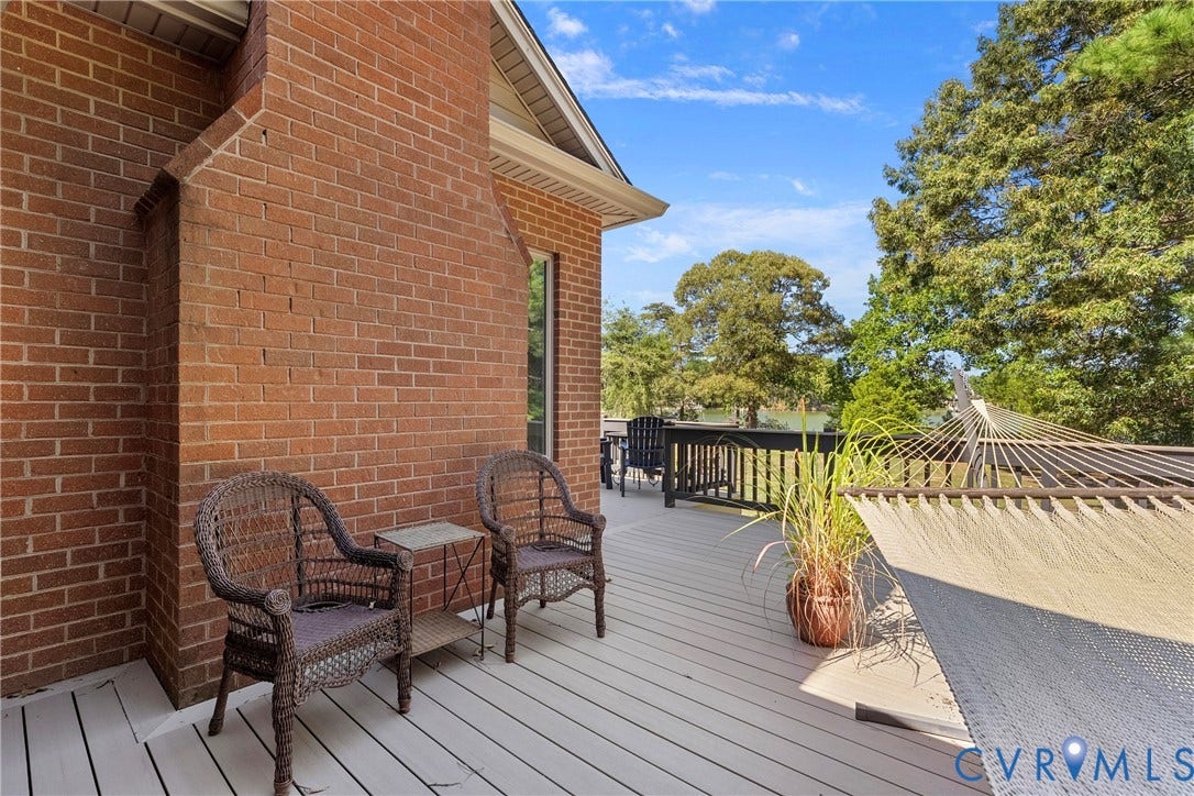 447 Tranquility Road, Reedville, VA 22539 Expansive outdoor deck featuring composite decking, a brick exterior wall, and surrounding mature trees