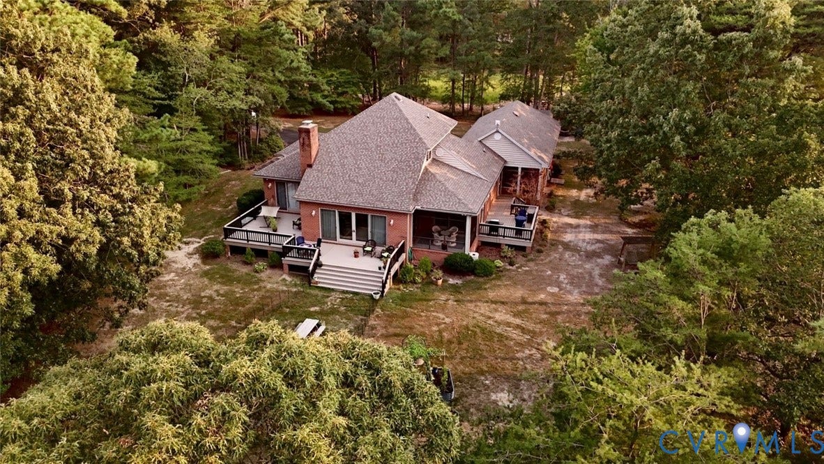 447 Tranquility Road, Reedville, VA 22539 Brick exterior residence with multi-level decks, mature tree surroundings, an asphalt driveway, and a covered porch