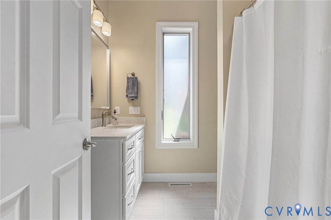 447 Tranquility Road, Reedville, VA 22539 White paneled door, single vanity with light-colored countertop, wall-mounted mirror, brushed nickel faucet, and a frosted vertical window