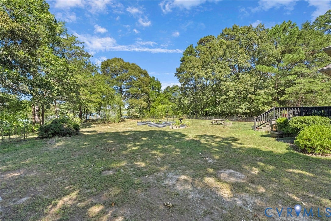 447 Tranquility Road, Reedville, VA 22539 Expansive lawn area with mature trees, a raised garden bed, and a wooden deck with stairs