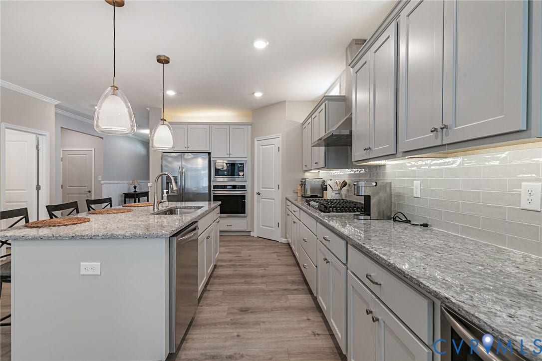 8681 Terroir Lane, Cottages At Viniterra, New Kent, VA 23124 Kitchen featuring an island with a built-in sink, stainless steel appliances, light gray cabinetry, light-toned countertops, and wood-finish flooring