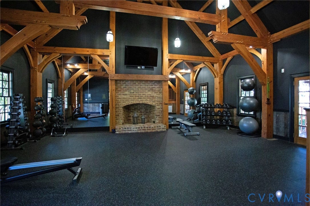 8681 Terroir Lane, Cottages At Viniterra, New Kent, VA 23124 Vaulted ceiling with exposed wood beams, brick-clad fireplace, large windows with dark trim, rubberized flooring, and built-in wall mirror