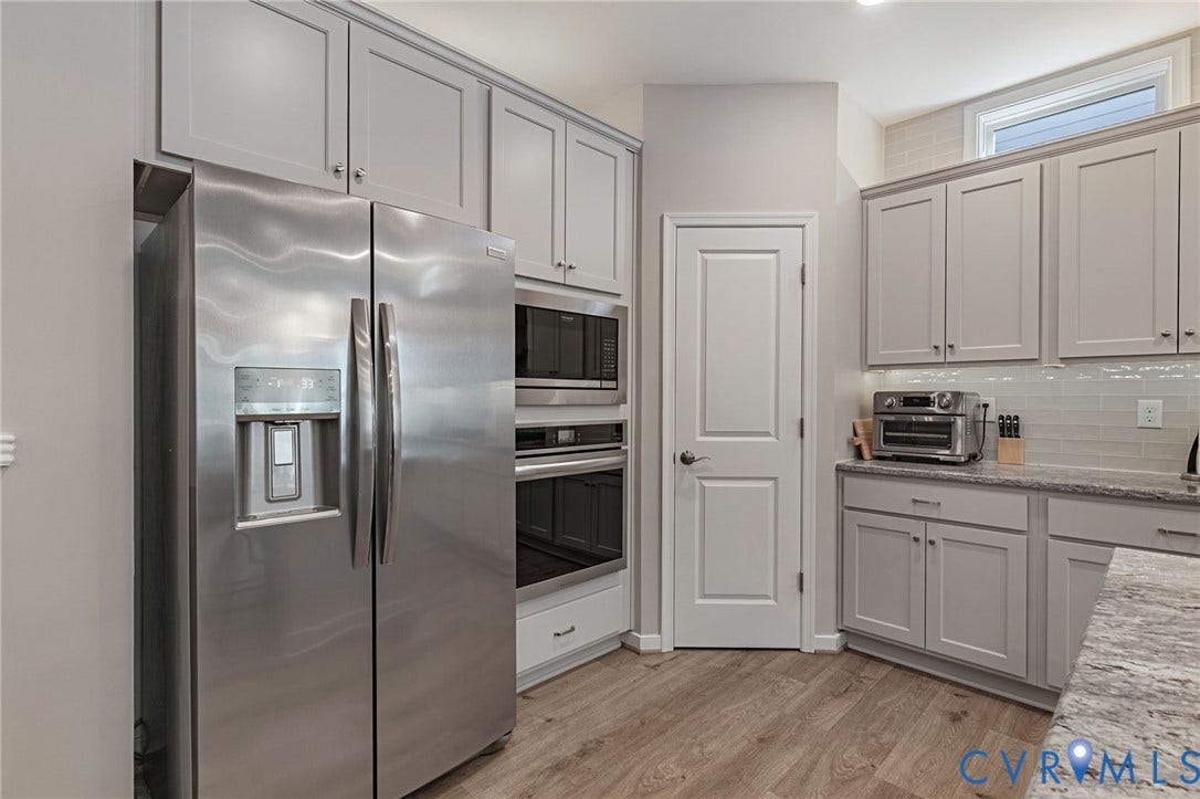 8681 Terroir Lane, Cottages At Viniterra, New Kent, VA 23124 Stainless steel side-by-side refrigerator, built-in double ovens, light gray shaker-style cabinetry, LVP flooring, and light-toned countertop