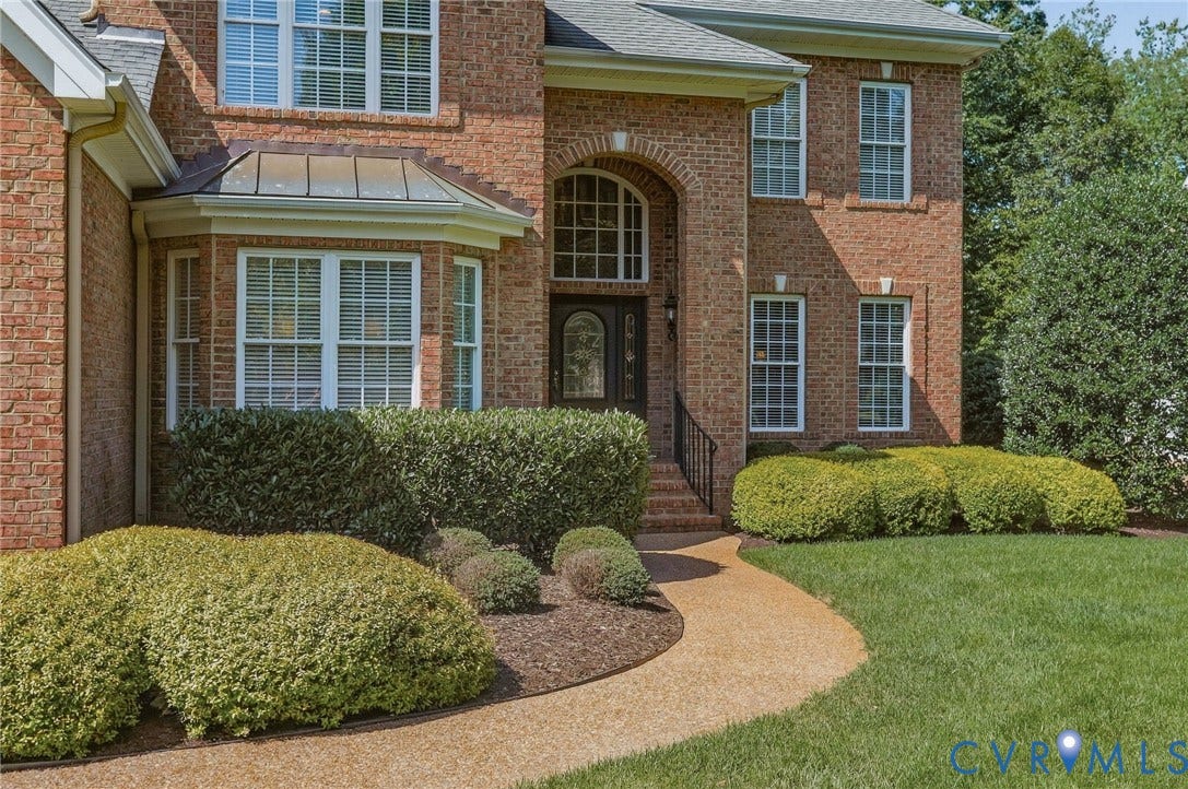 3012 Hedgeway Place, Tarrington, Midlothian, VA 23113 Brick exterior featuring a bay window with a metal roof accent, an arched entryway, a stone pathway, and mature landscaping