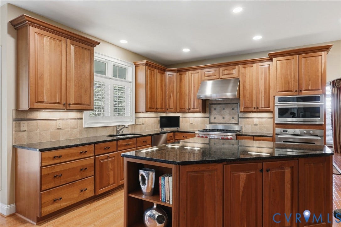 3012 Hedgeway Place, Tarrington, Midlothian, VA 23113 Kitchen featuring wood cabinetry, dark countertops, a large island with shelving, stainless steel appliances, and a tiled backsplash