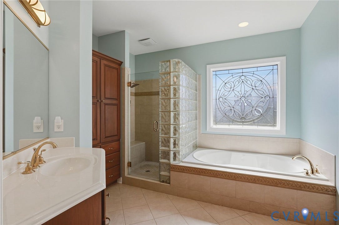 3012 Hedgeway Place, Tarrington, Midlothian, VA 23113 Soaking tub with decorative tile surround, walk-in shower with glass block accent, custom stained-wood cabinetry, and an ornate leaded-glass window